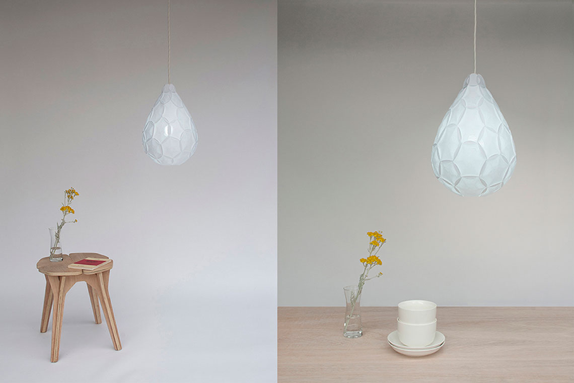 Airy Small teardrop white suspension lamp is shown with plywood stool and Airy Small lamp is suspended over a dining wood table with white cups and a flower vase