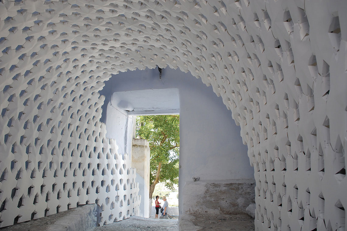 View of Daphne Installation completed by 24d-studio showing self-supporting white paper panel arch situated within a tunnel in Pyrgos, Greece.
