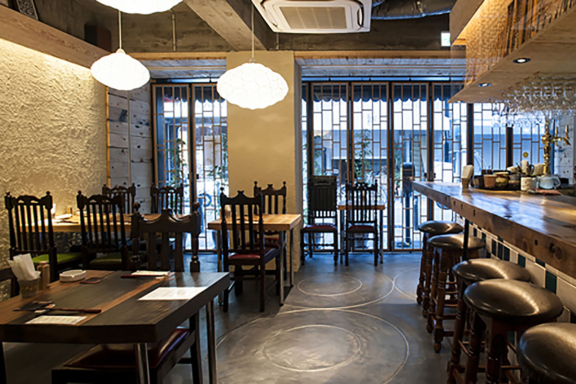 Airy white pendant lamp collection is installed in Kobe restaurant. The background shows dark wood table counter on the right and wood tables and chairs on the right.