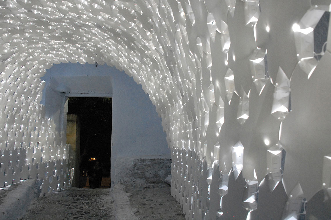 Photo showing a detail of Daphne installation paper panel arch assembly with lights on during night time.