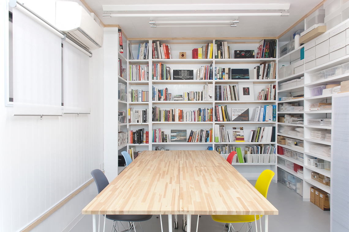 Kobe Studio view of library and meeting room with built-in shelves and mobile conference table.